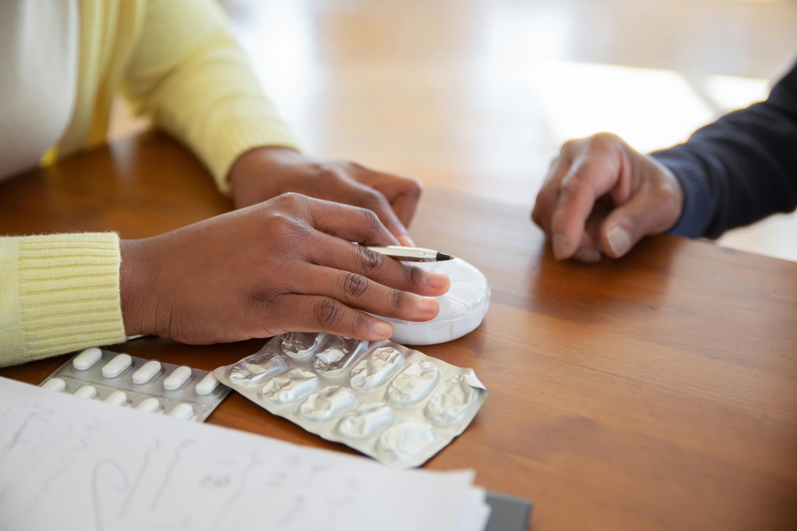 Detail view of hands with medication and pen on a wooden table.